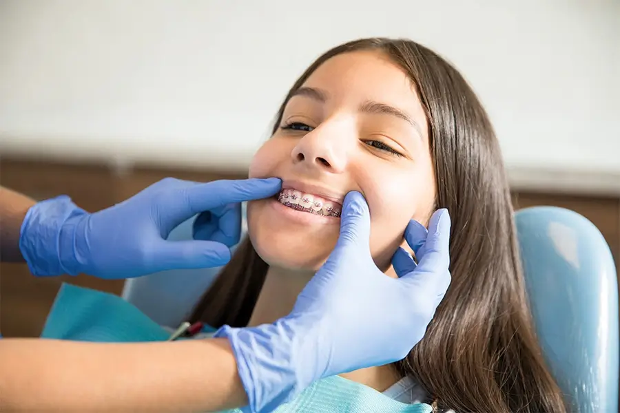 Dentist’s gloved hands showing a smiling teen girl’s metal braces during an orthodontic checkup
