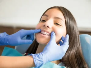 Dentist’s gloved hands showing a smiling teen girl’s metal braces during an orthodontic checkup